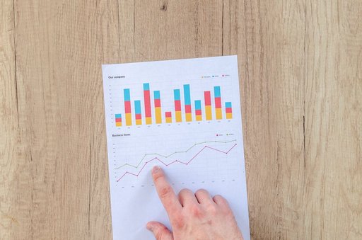 Tangan seorang pebisnis menunjuk pada berbagai grafik di atas kertas, menggambarkan data dan analisis keuangan.